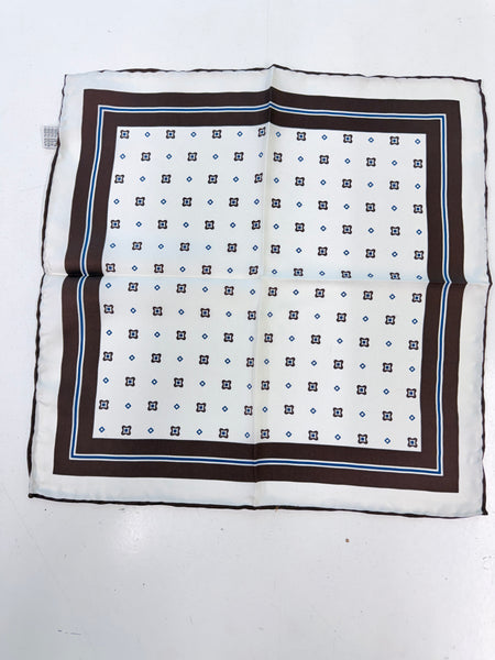A square scarf with a geometric pattern, featuring a white center with small black and blue diamond motifs, surrounded by a wide brown border and a thin light blue stripe, laid flat on a white surface.
