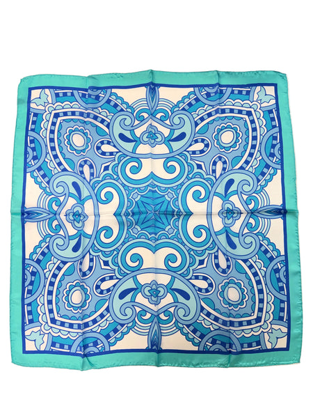 A square silk scarf with an intricate blue and white mandala pattern and a turquoise border, laid flat on a white table.