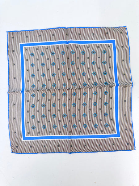 A square patterned scarf laid flat on a white background. The scarf features a gray and white striped center with blue diamond motifs, bordered by a white inner border and a vibrant blue outer border.